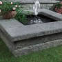 Bruchsteinmauer mit Abdeckplatte in Grau-Nuanciert und kleinem Springbrunnen im Garten.