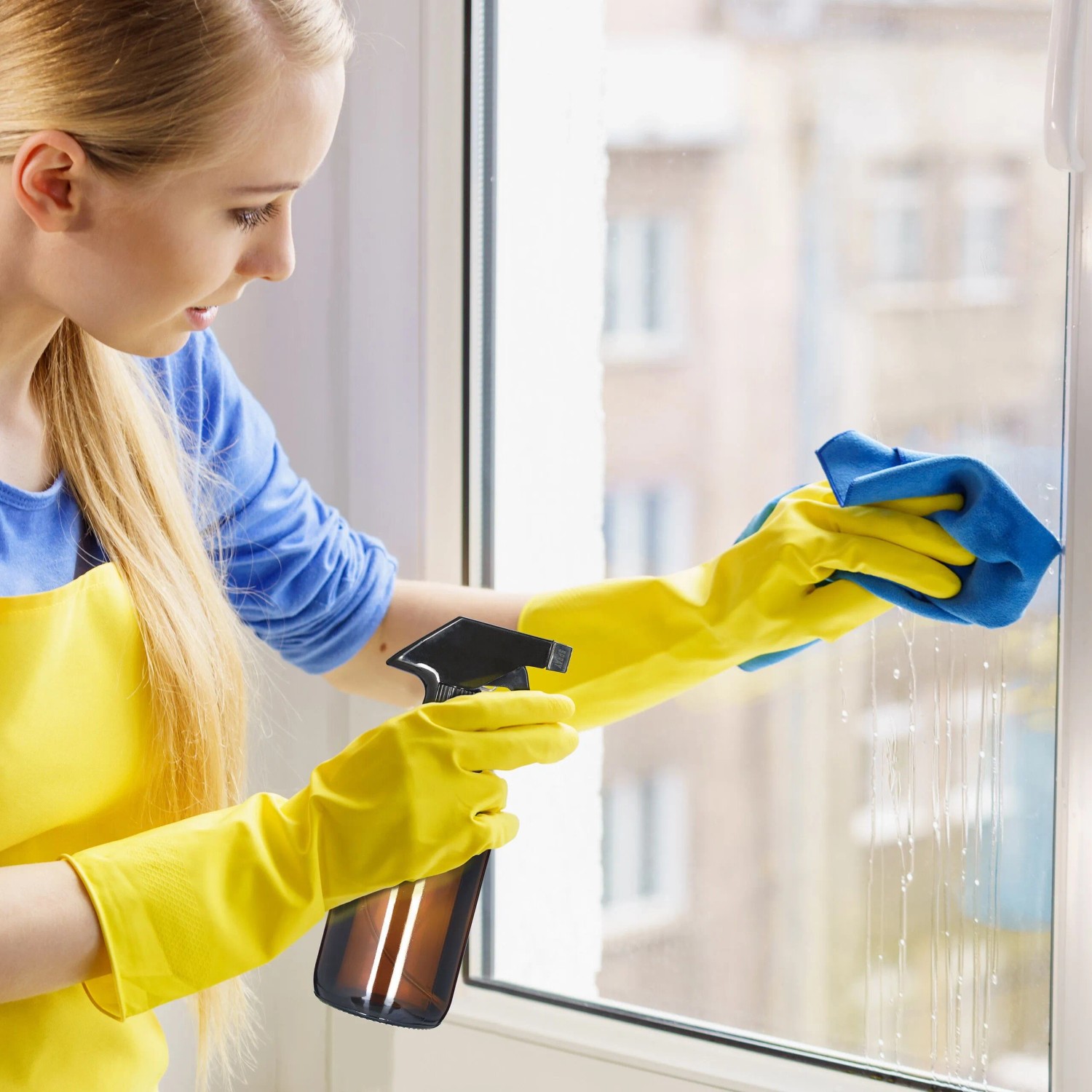 Frau reinigt Fenster mit brauner Relaxdays Sprühflasche (4er Set) und gelben Handschuhen.