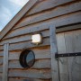 Quadratische Lutec LED Solar-Wandleuchte Curtis mit Bewegungsmelder an Holzwand.