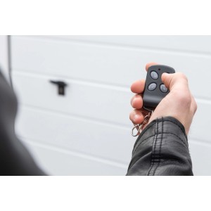 Hand mit Schellenberg 4-Kanal Handsender vor Garagentor. Fernbedienung für Torantriebe.