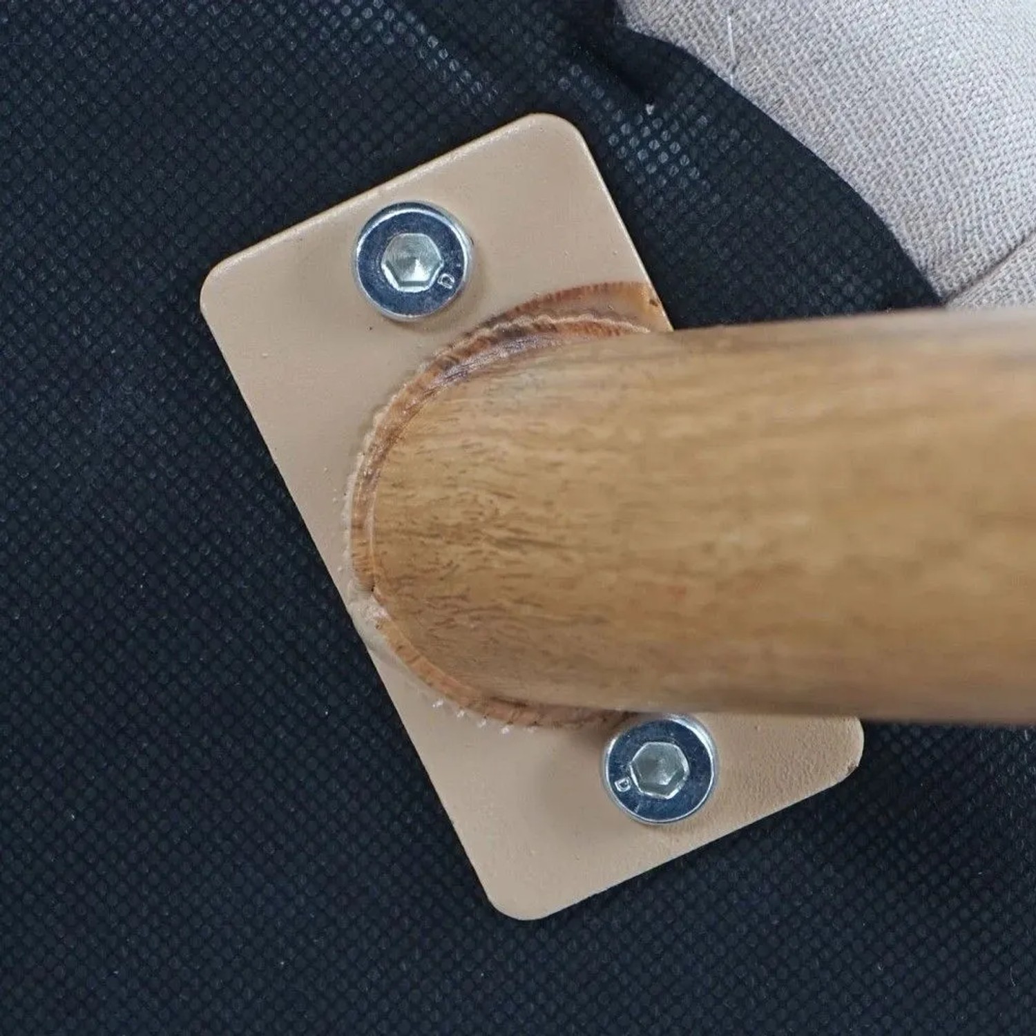 Detailansicht der Stuhlbeinbefestigung: Metallbein in Holz-Optik, beige Platte mit Schrauben am Stoffbezug des Esszimmerstuhls.