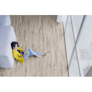 Kaindl Laminat Masterfloor Oak Blackwood, 7mm. Frau liest auf dem Laminatboden neben einem Fenster.