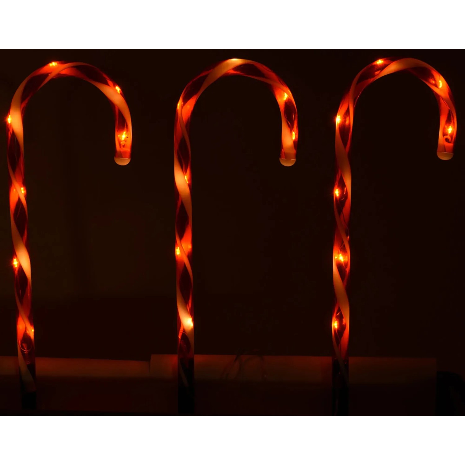 Drei leuchtende Zuckerstangen mit rot-weißem Spiralmuster als Weihnachtsdekoration.