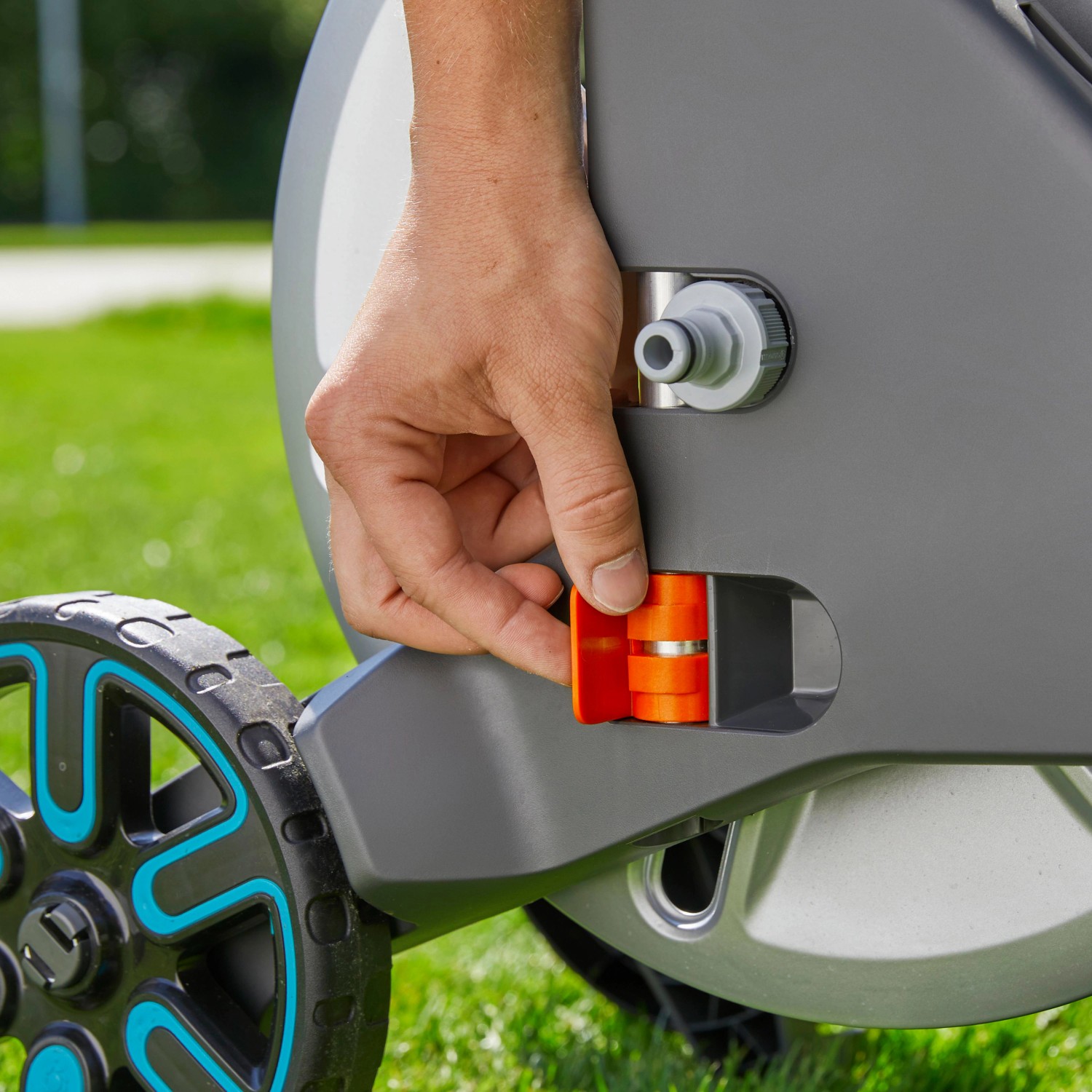 Detailaufnahme: Hand bedient orangefarbenen Mechanismus am Gardena Aqua Roll M Schlauchwagen Set.