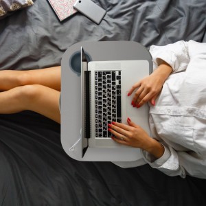 Graues Relaxdays Laptopkissen mit Getränkehalter auf dem Schoß einer Person im Bett, die einen Laptop nutzt.