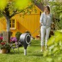 Gardena RollUp S 15 m Gartenschlauchbox mit Frau beim Bewässern im Garten vor gelbem Haus.