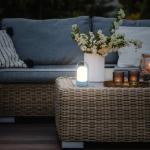 Blaue Brilo Akku-LED-Tischleuchte auf Gartentisch, warmweißes Licht für gemütliche Atmosphäre.