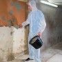 Mann verputzt Wand mit Einwegoverall XL als Schutz.