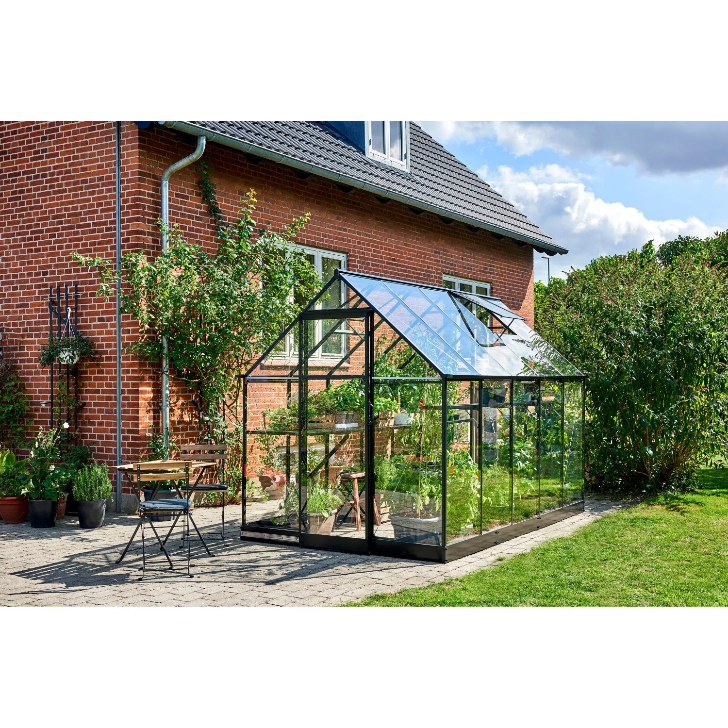 Schwarzes Halls Gewächshaus Qube 610 mit Glasfront im Garten.