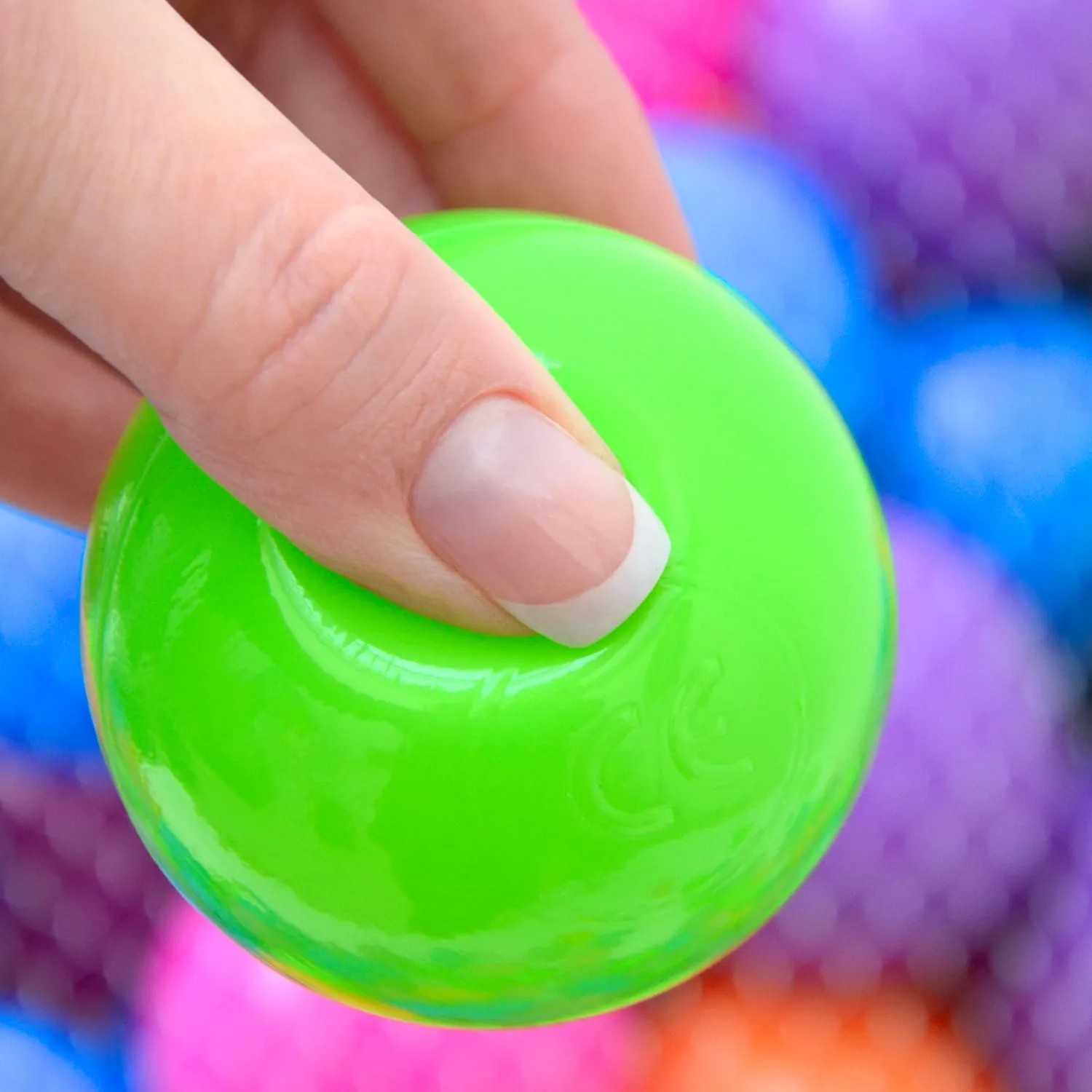 Hand drückt grünen LittleTom Bällebadball (Ø 6cm) aus Pastell Set. Spiel & Spaß für Kinder.