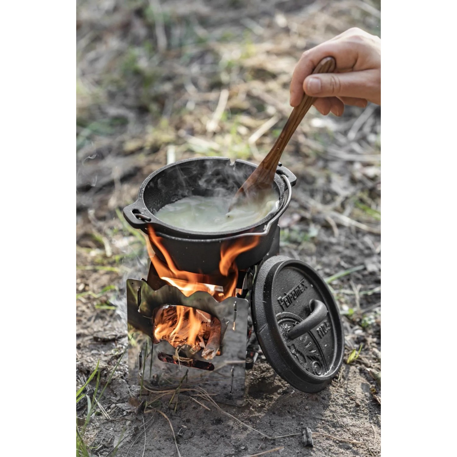 Petromax Hobo-Kocher bk1 aus Edelstahl im Einsatz mit Topf und Kochlöffel. Grillutensil für Outdoor-Küche.