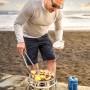 Petromax Atago Gasgrill-Set: Edelstahl Grill mit Person am Strand beim Grillen von Garnelen.