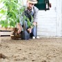Schwarzer Relaxdays Schlauchaufroller aus Stahl, wandmontiert, mit Person beim Pflanzen im Garten.