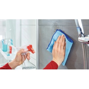 Anwendung der Tesa Powerstrips Klebehaken: Reinigung von Fliesen mit Reiniger und Tuch im Badezimmer.