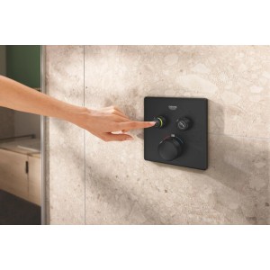 Schwarzes, eckiges Grohe SmartControl UP-Thermostat an gefliester Wand. Hand bedient Knopf mit grünem Ring zur Duschsteuerung.