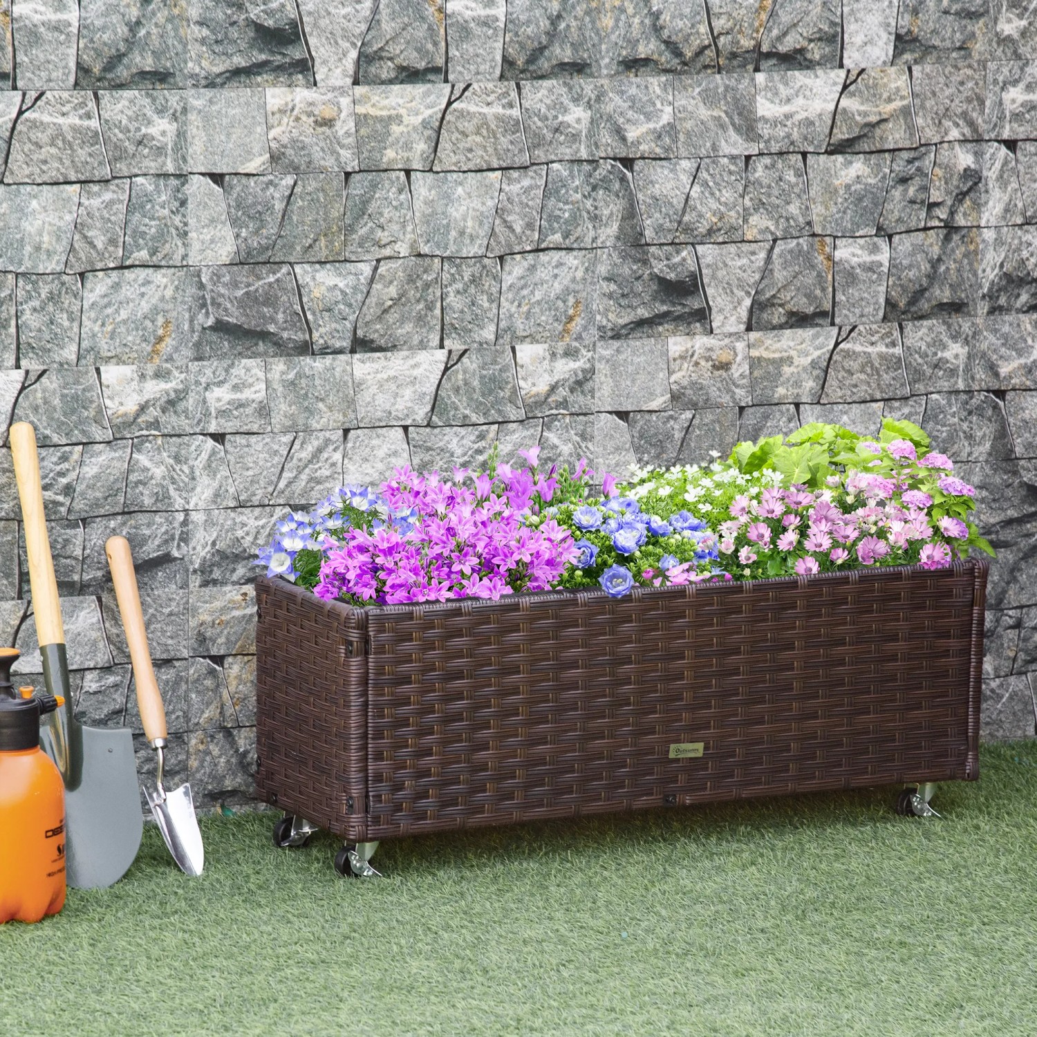 Braunes Outsunny Rattan Hochbeet mit Blumen und Rädern vor Steinwand.