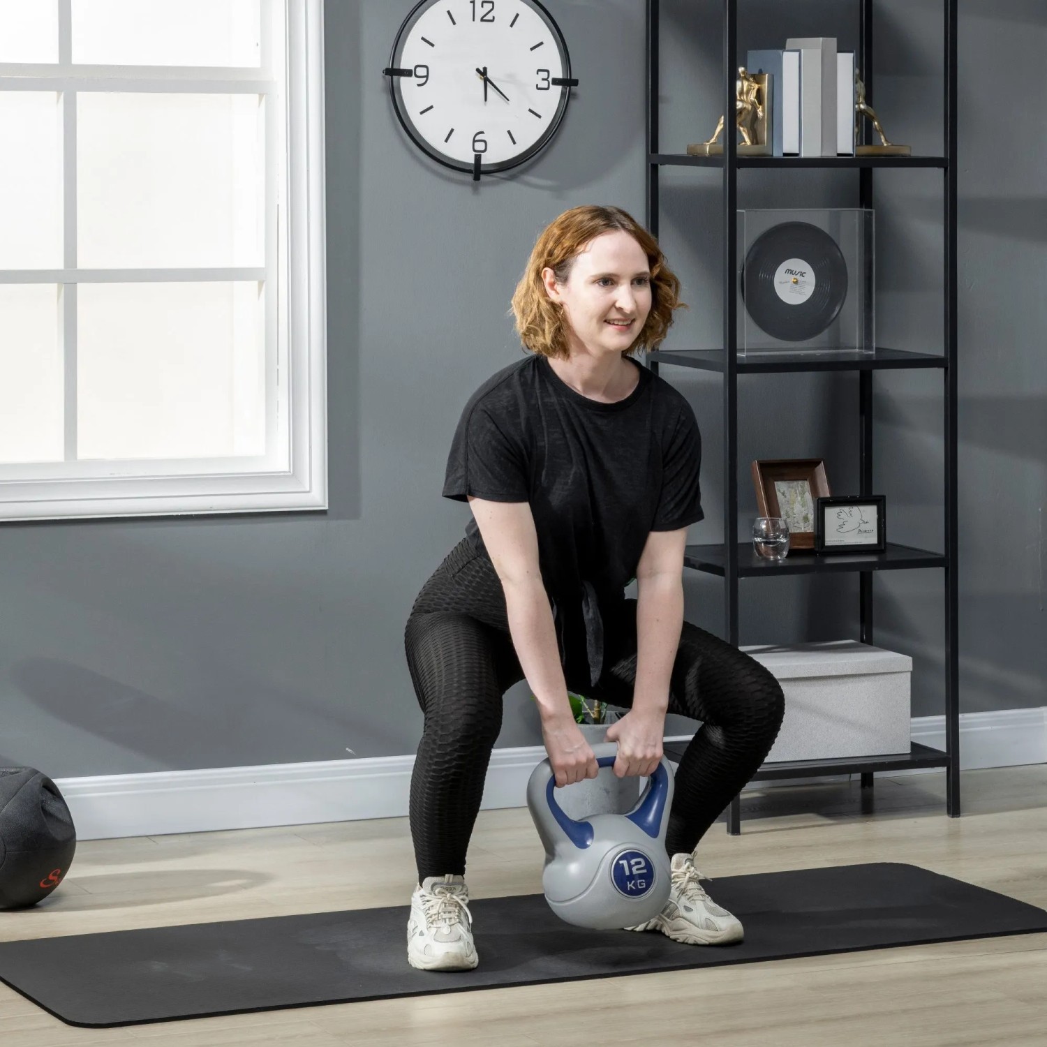 Frau macht Kniebeugen mit blauer 12 kg SPORTNOW Kettlebell auf Fitnessmatte. Ideales Gewichtstraining.