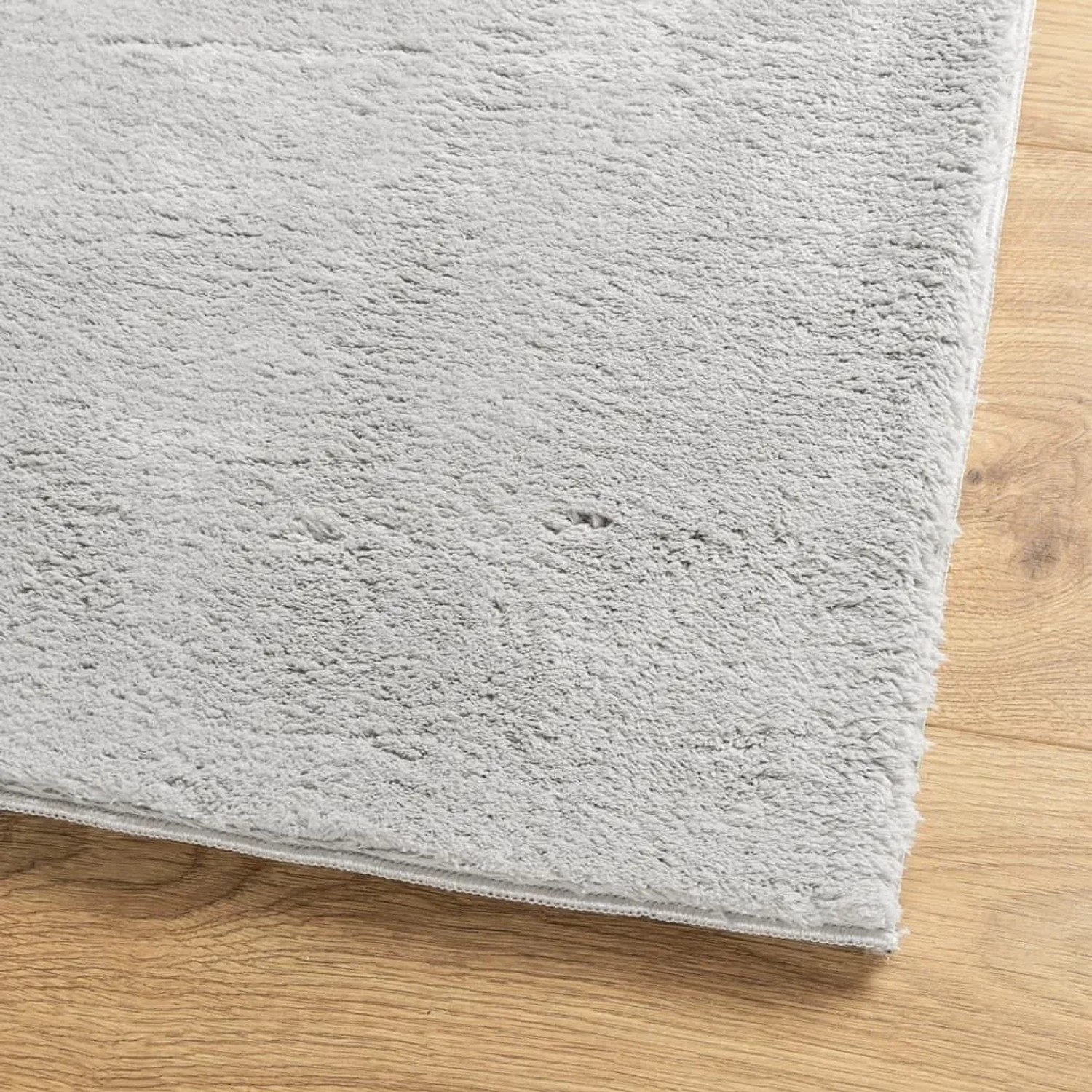 Grauer, weicher Kurzflor-Teppich aus Polyester mit flauschiger Oberfläche auf Holzfußboden. Waschbar.