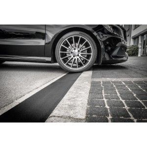 Schwarze Bordsteinrampe aus Gummigranulat unter einem PKW-Reifen.