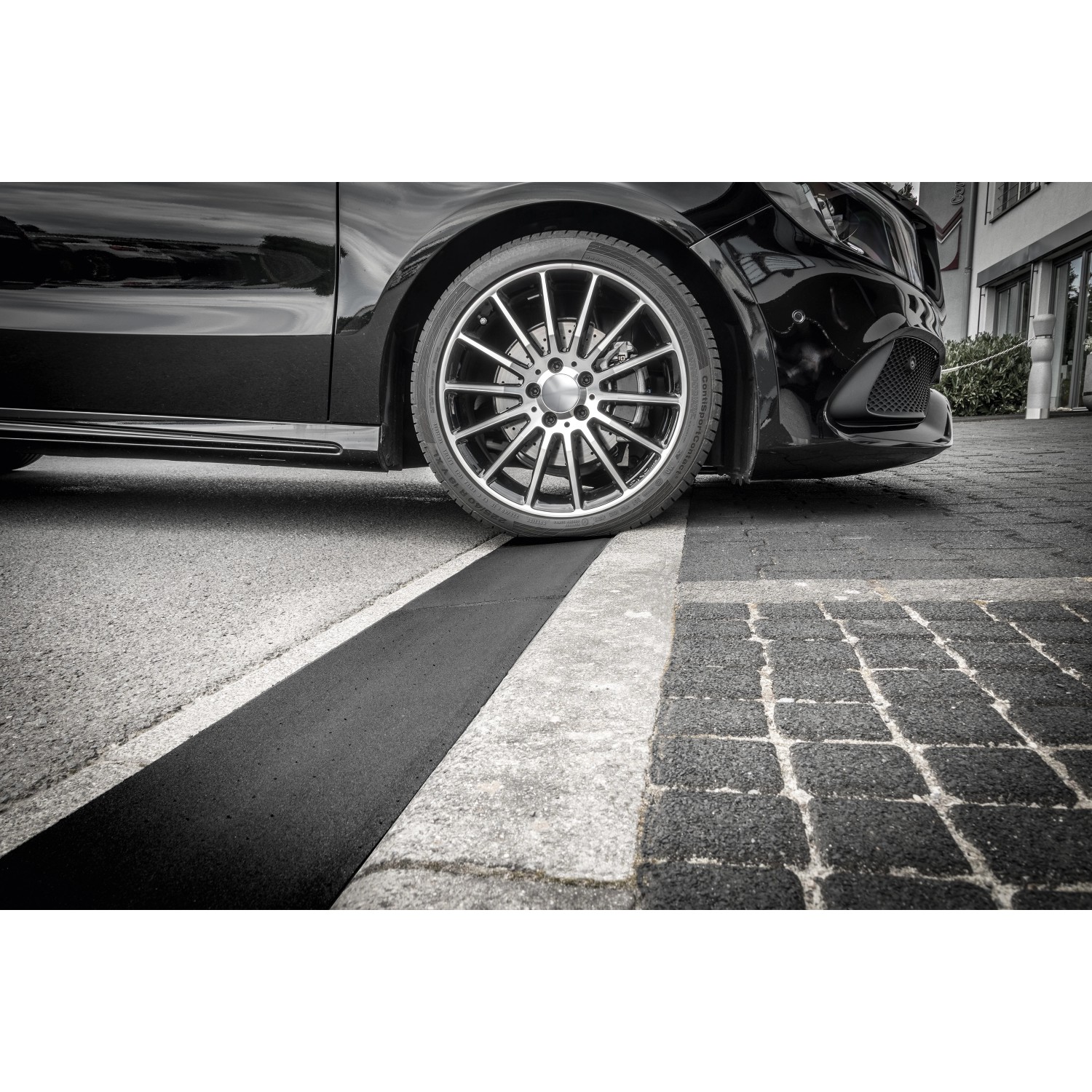 Schwarze Bordsteinrampe aus Gummigranulat unter einem PKW-Reifen.