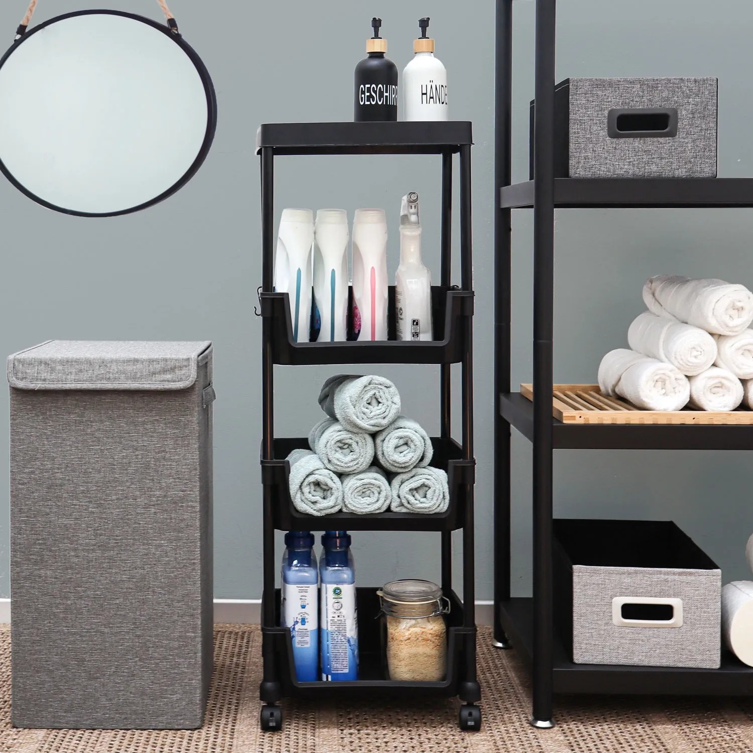Schwarzer MAKLIK Küchenrollwagen mit 3 Körben (35x24x100 cm) im Badezimmer mit Handtüchern und Pflegeprodukten.