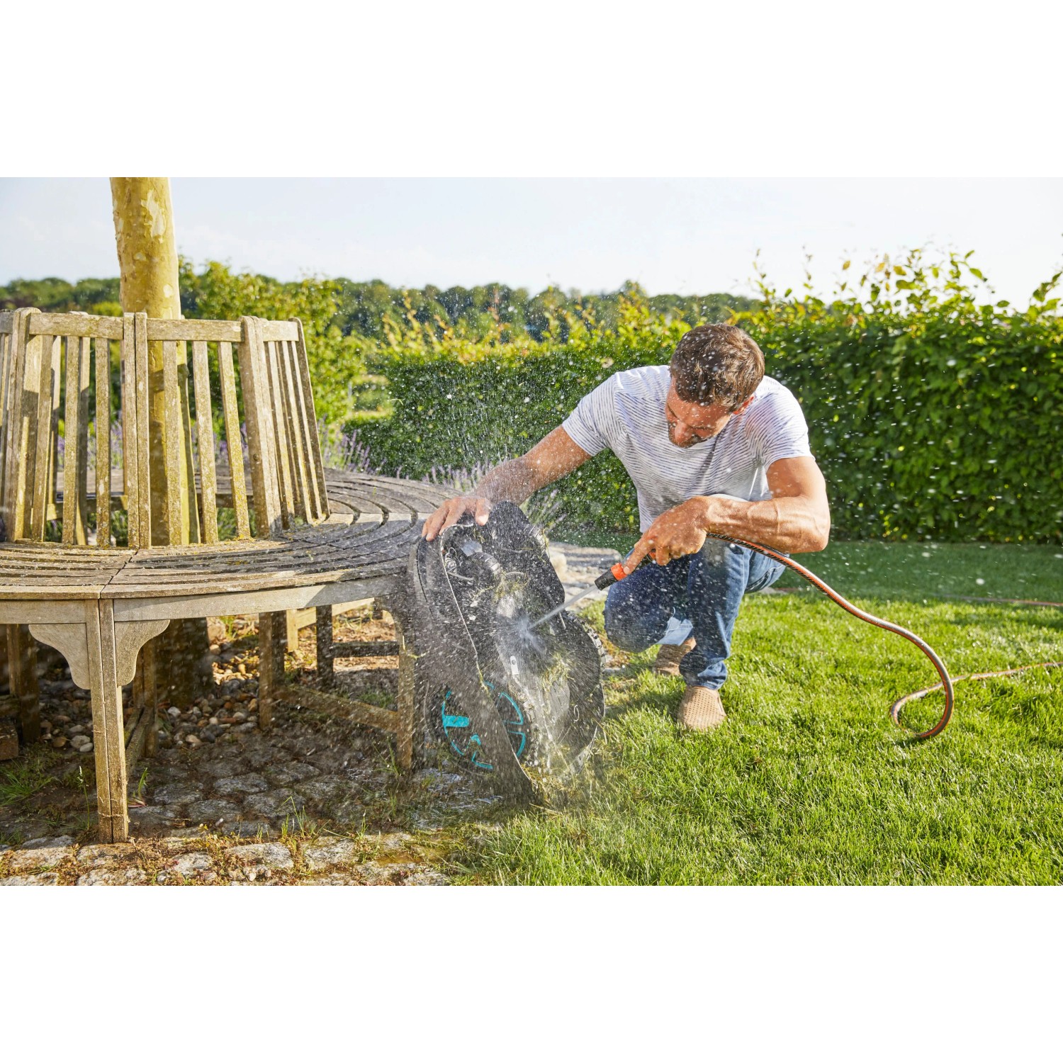 Mann reinigt Gardena smart Sileno life Mähroboter mit Wasserschlauch im Garten.