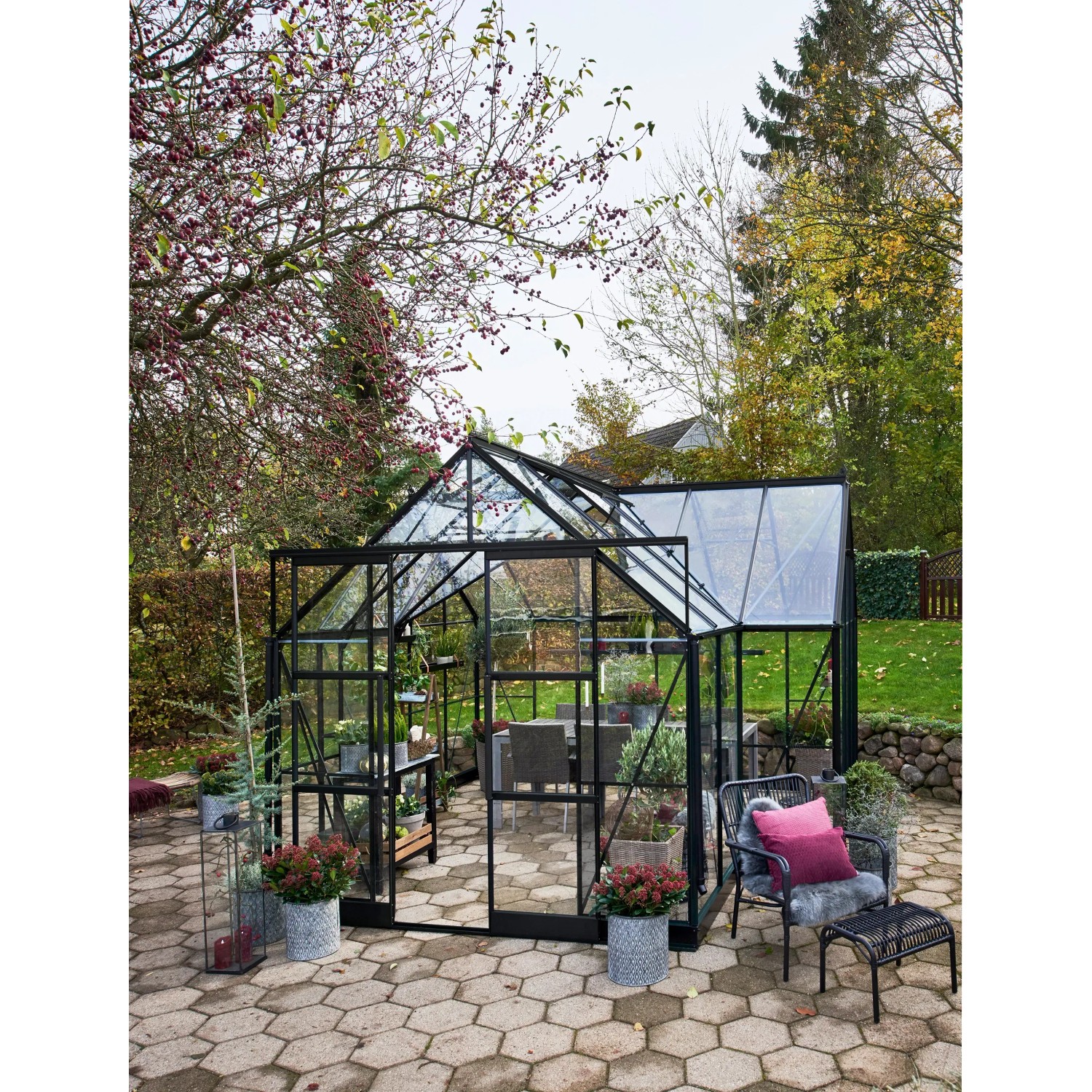Schwarzes Halls Gewächshaus Garden Room 12,9 m² im Garten mit Pflanzen und Sitzbereich.