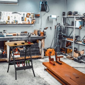 Klappbare Werkbank aus schwarzem Stahl mit heller Holzplatte, Spannbacken und Werkzeughalterung in Werkstatt.