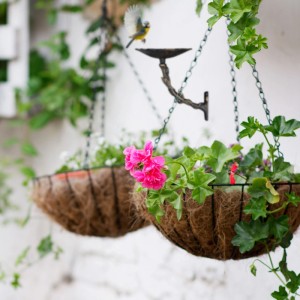 Weiße Relaxdays Vogeltränke aus Gusseisen mit Blumenmuster und zwei bepflanzten Hängekörben.