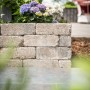 Diephaus Mauerstein Collo Muschelkalk, 30x10x10 cm, als kleine Gartenmauer mit Blumen im Hintergrund.