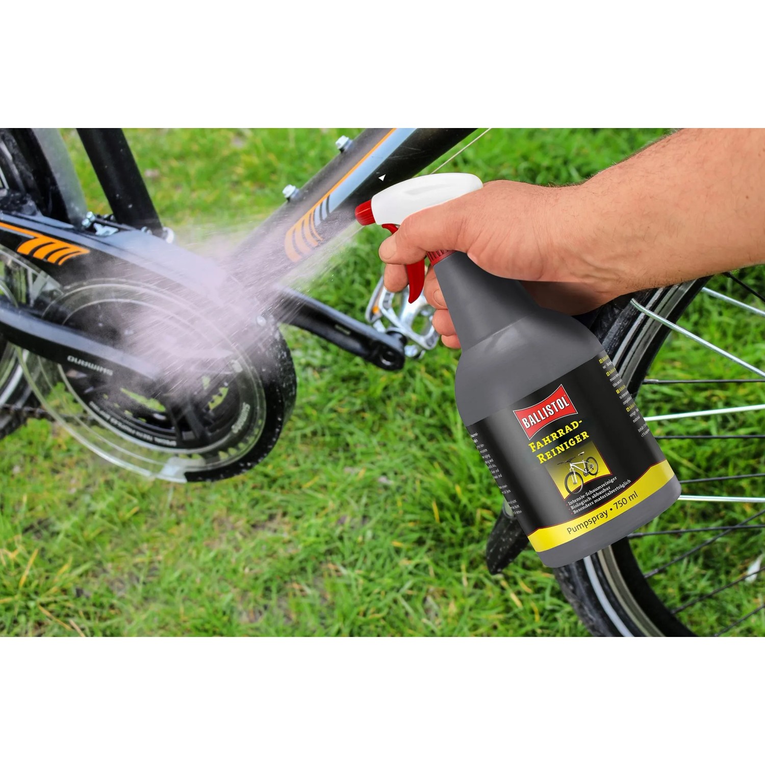Hand sprüht Ballistol Fahrrad-Reiniger 750 ml auf Fahrradkette. Graue Flasche reinigt Fahrrad im Gras.