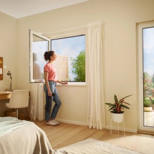 Frau öffnet Fenster mit tesa Insect Stop Fliegengitter Premium in Weiß. Effektiver Insektenschutz.
