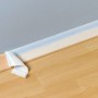 Beiges Flachkrepp Klebeband wird von einer hellblauen Wand über Holzfußleiste und Boden abgezogen, zeigt saubere Kante.