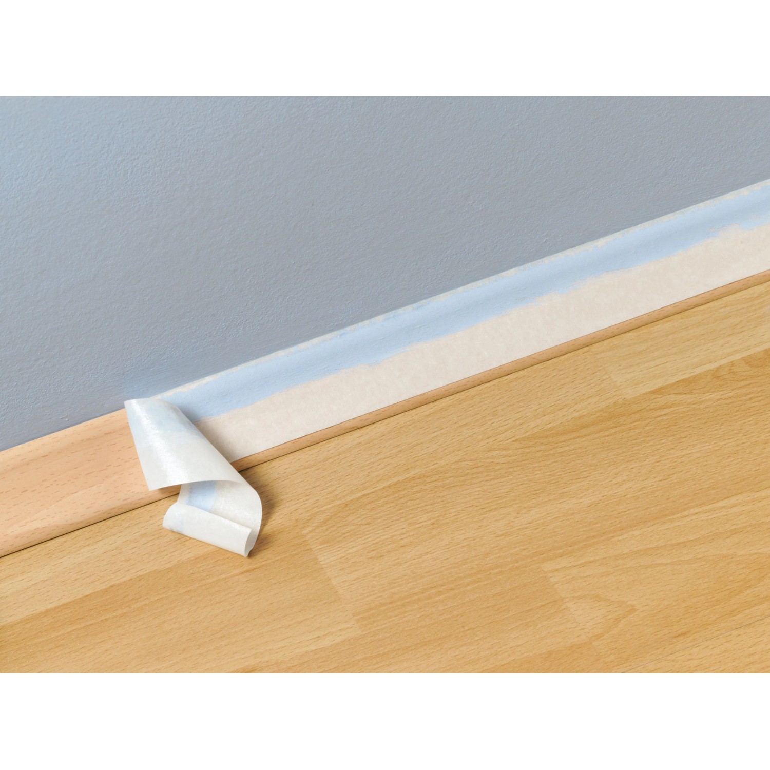 Beiges Flachkrepp Klebeband wird von einer hellblauen Wand über Holzfußleiste und Boden abgezogen, zeigt saubere Kante.