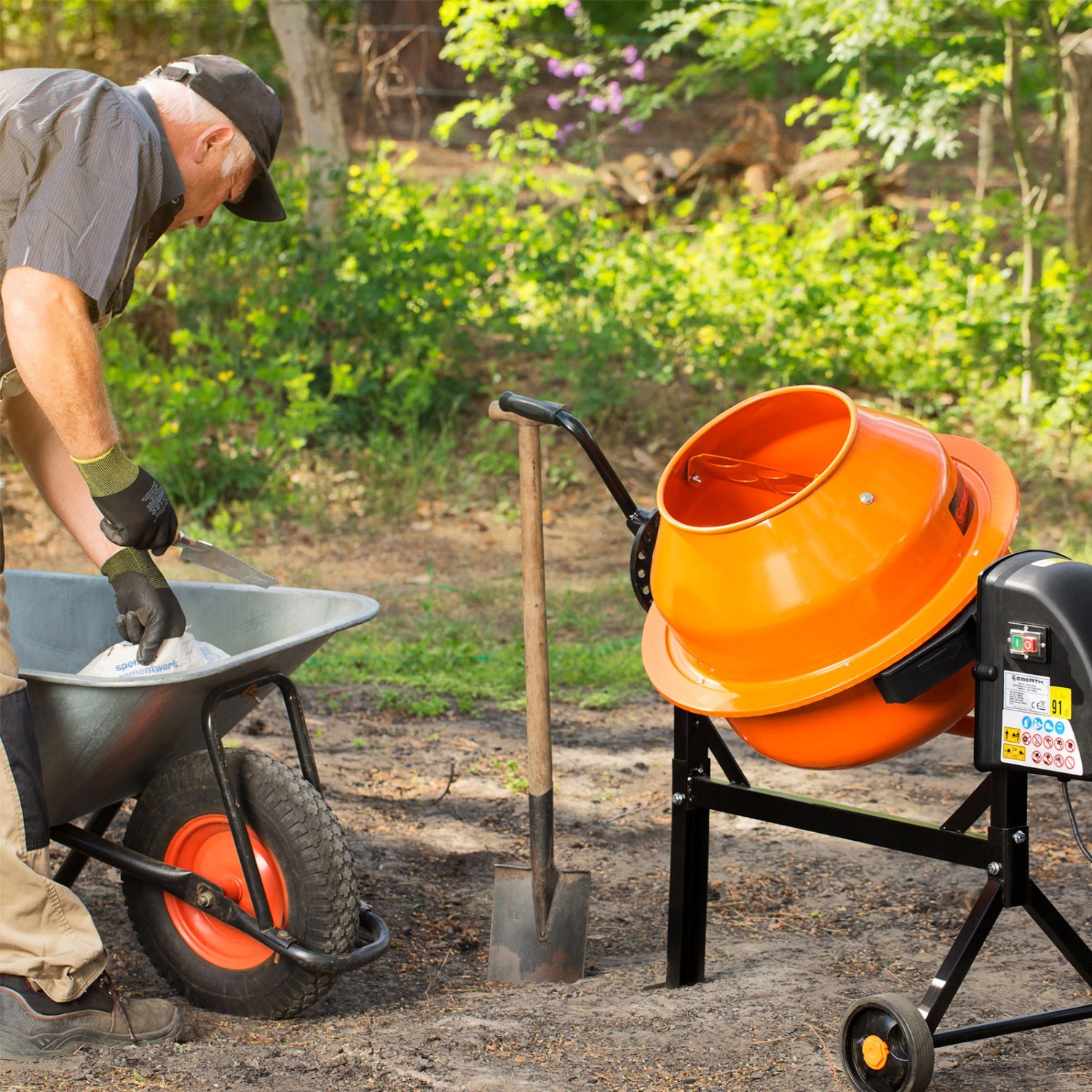 EBERTH 65L Betonmischer in Aktion: Mann befüllt Schubkarre neben dem orangefarbenen Mischer.