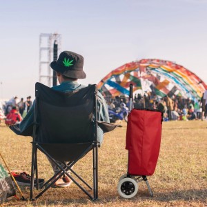 Roter Relaxdays Einkaufstrolley aus Stoff und Stahl neben Person auf Festival. Faltbarer Trolley mit 2 Rädern.