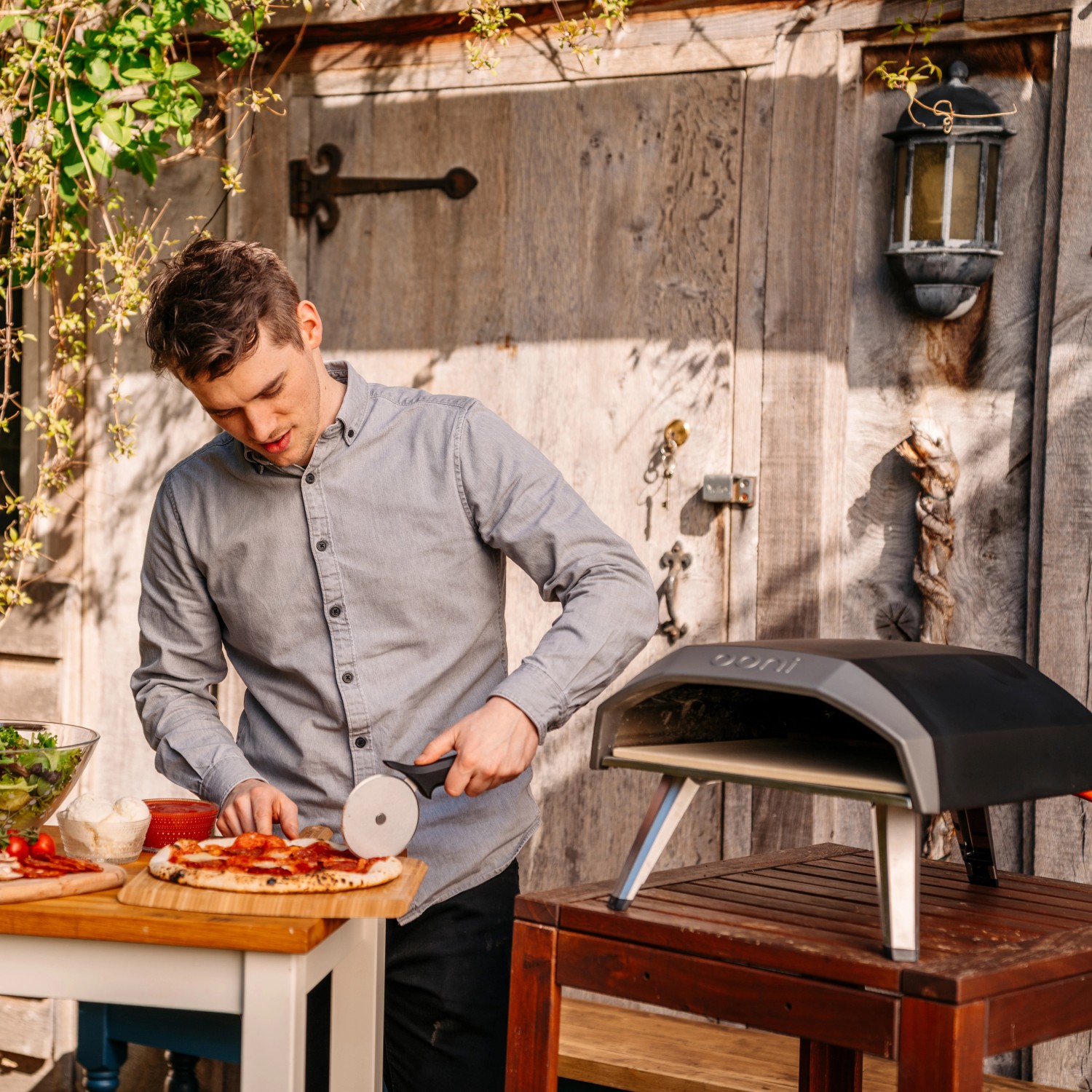Mann schneidet Pizza neben Ooni Koda 12 Gas-Pizzaofen. Kompakter Gasgrill für leckere Pizza.