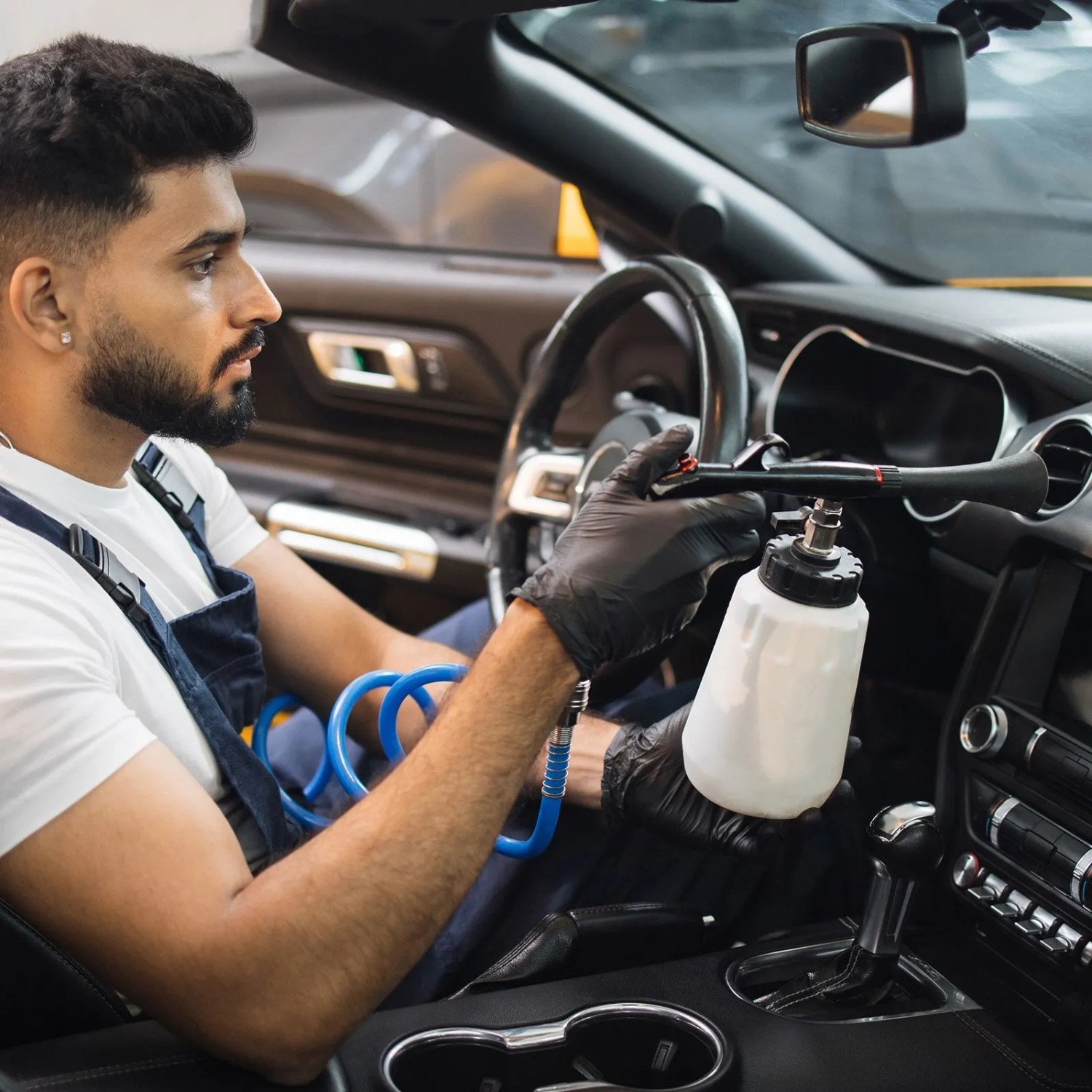 Mann nutzt blauen Spiraldruckluftschlauch (5m, 1/4 Zoll) für Druckluftwerkzeug im Auto. Ideal für Kompressor in der Werkstatt.