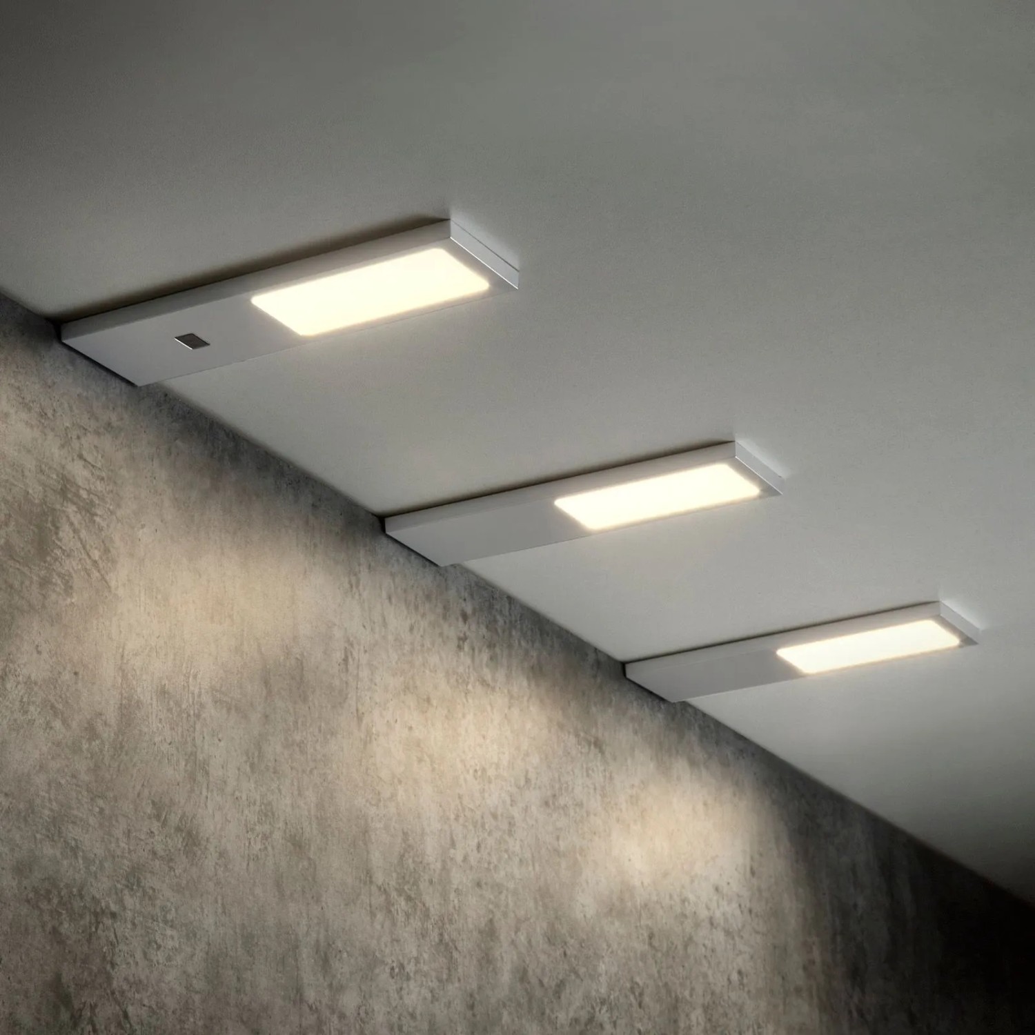 Drei flache SOTECH GIULIA II LED-Unterbauleuchten, silbergrau, warmweiß leuchtend, eine mit Sensor.