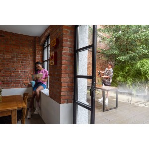 Kärcher Hochdruckreiniger K Silent: Person reinigt Tisch im Außenbereich, während eine andere Person im Innenbereich liest.