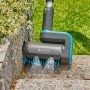 Gardena Akku-Multi-Reiniger AquaBrush Patio im Einsatz mit Wasserstrahl an Steinmauer.