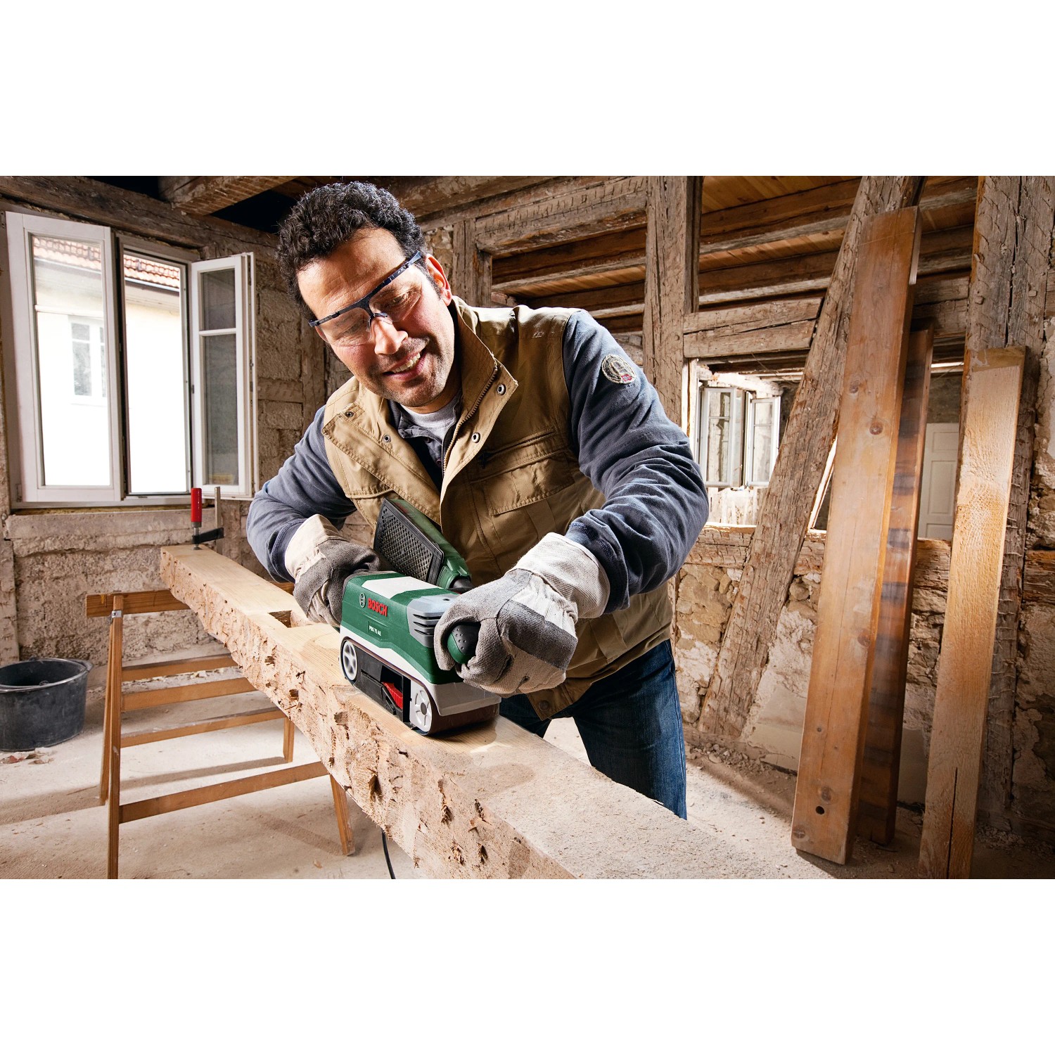 Mann schleift Holzbalken mit Bosch Bandschleifer PBS 75 AE Set (750 W) in Werkstatt.