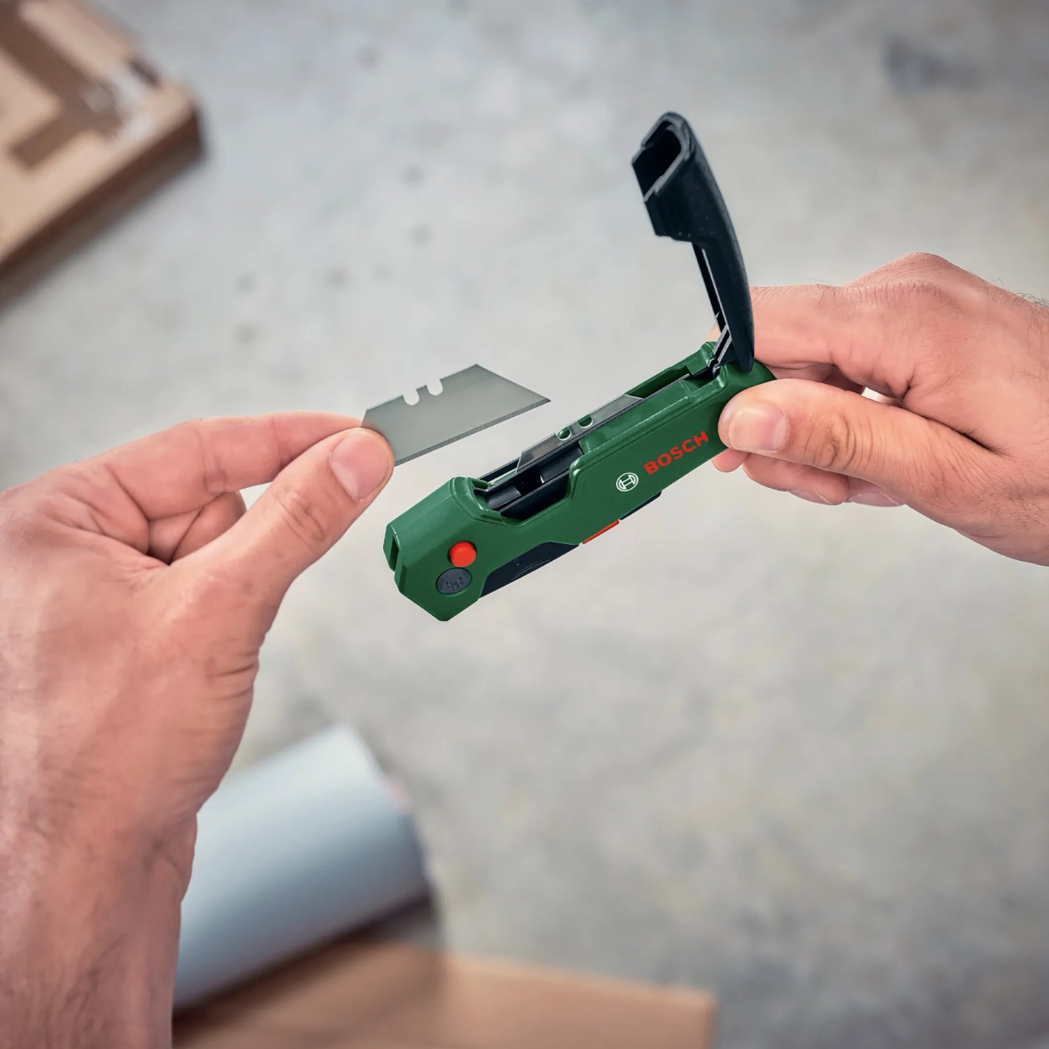 Bosch Klappmesser: Hand legt Klinge in grünes Cuttermesser mit Klingenfach.