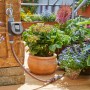 Gardena Bewässerungscomputer Flex am Wasserhahn mit Pflanzen im Hintergrund.