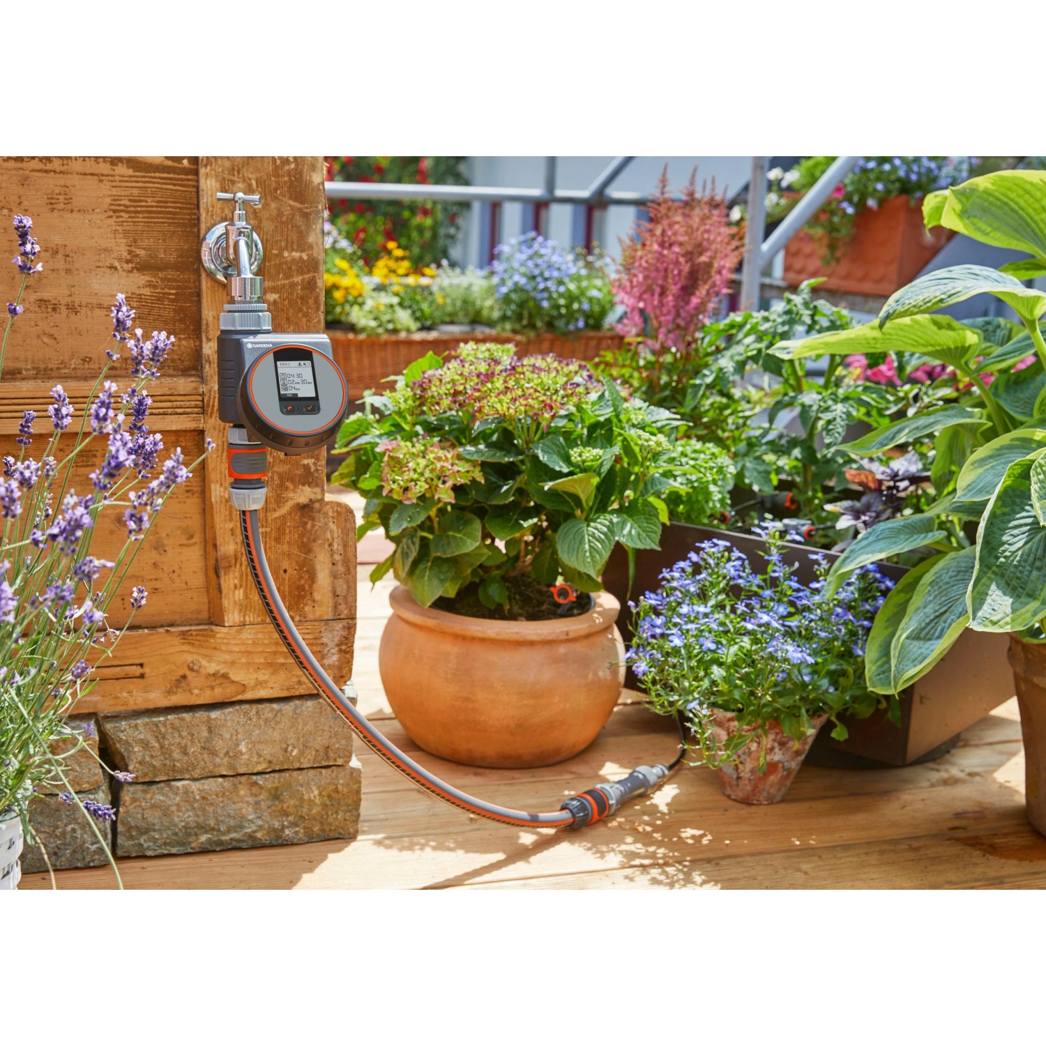 Gardena Bewässerungscomputer Flex am Wasserhahn mit Pflanzen im Hintergrund.