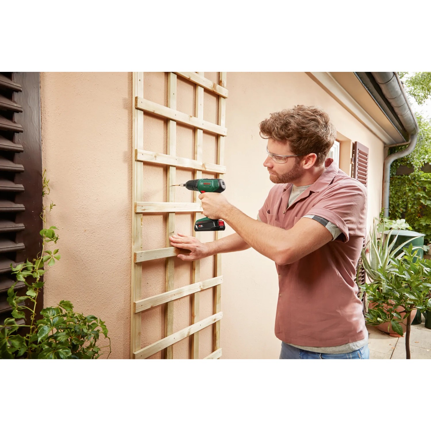 Bosch EasyDrill 18V-38 Akkuschrauber im Einsatz beim Schrauben eines Holzspaliers an einer Hauswand.