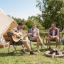 Personen sitzen auf Rattan Gartenstühlen von Sekey. Camping Szene mit Zelt und Gitarre.
