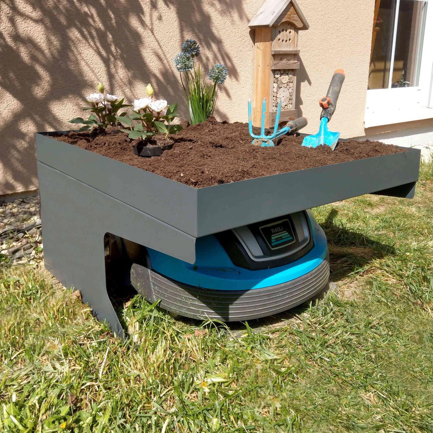 Anthrazitfarbene Mähroboter-Garage G60 mit Pflanzkasten und Mähroboter im Garten.