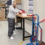 Mann verpackt Ware auf höhenverstellbarer rikta Werkbank mit Holzplatte und schwarzem Gestell.