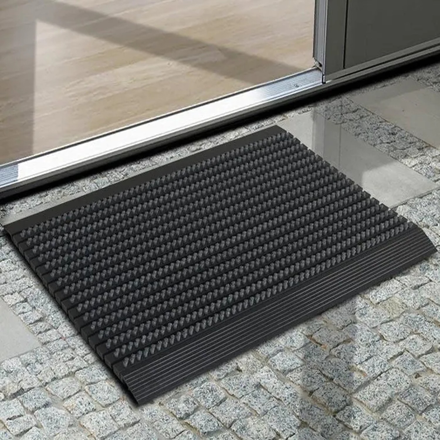 Graue Karat Fußmatte Power Brush mit Bürsten, 40x60 cm, vor einer Tür. Fußabtreter für Innen und Außen.